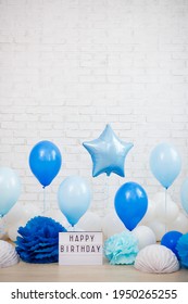 Birthday Party Concept - Blue And White Air Balloons, Paper Balls And Lightbox With Happy Birtday Text Over Brick Wall With Copy Space