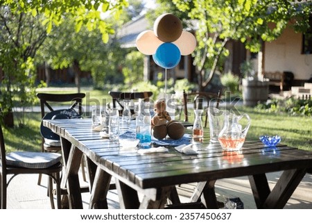 Birthday party. An empty table with glasses and a teddy bear with balloons.