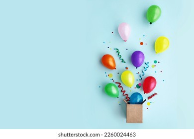 Birthday party flat lay with colorful balloons and confetti escaping from a gift box
