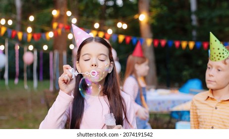 Birthday party. Small children wearing party hat playing with bubbles in garden in summer outdoors. Holiday atmosphere concept  - Powered by Shutterstock