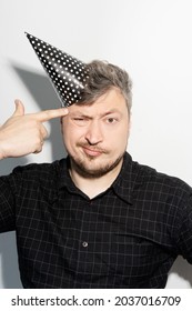 Birthday Problem. Celebrating Difficulty. Organizational Worry. Confused Insecure Guy In Festive Party Hat With Shooting Hand Gesture Isolated On White Studio Background.