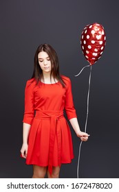 Birthday Is A Sad Holiday, Regret For Growing Up. A Girl In A Red Dress On A Black Background Holds A Balloon In Her Hand And Is Sad On Her Birthday.