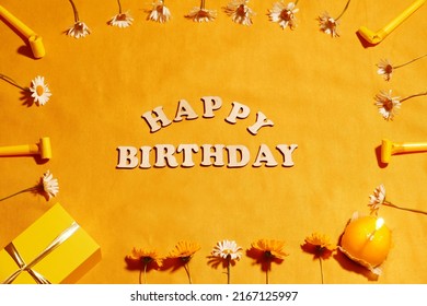 Birthday template on an orange background. Holiday pattern with different whistles, daisies, cupcake, gift box on yellow background. Flat lay. View from above. Birthday party decorations.