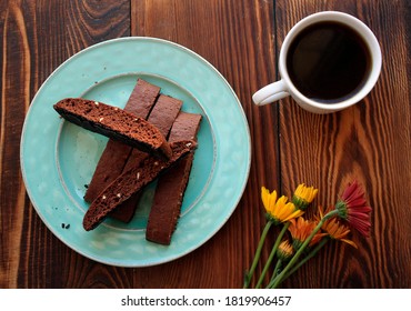 Biscotti cookies chocolate on green plate on a brown wooden background. White mug of coffee and fall daisy flowers. 