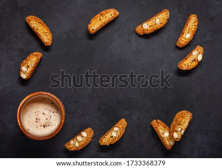 Biscotti on a black background. Frame made of a cup of cappuccino and cookies with almonds. Top view. Copy space.