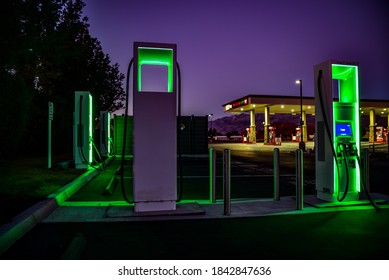 Bishop, California / USA - October 27 2020: Green Lights Of Electric Vehicle Charging Stations At Night And Gas Station