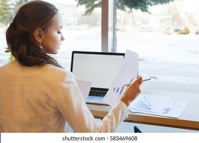 Bisnesswoman sitting at desk with computer and looking at chart on paper - Shutterstock ID 583469608