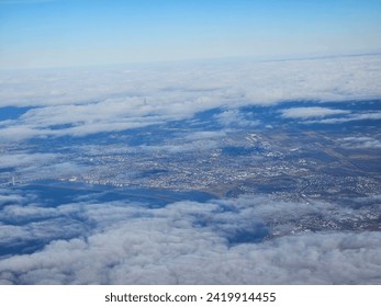A bit of  cloud cover hovering over a large populated area that is seen stretching out for miles from above.