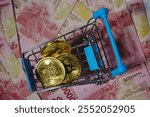 Bitcoin BTC Cryptocurrency Coin in a small shopping trolley with a hundred thousand Indonesian rupiah note in the background, close up. The concept of digital money and bitcoin.