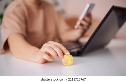 A bitcoin coin and a smartphone in a woman's hand against the background of graphs of growing incomes on monitors. Selective focus on Bitcoin - Shutterstock ID 2111713967
