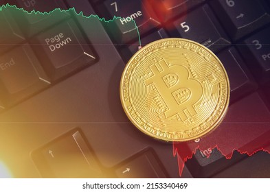 Bitcoin gold coin on a computer keyboard with a graph of the dollar exchange rate and the effect of sunlight. The concept of falling cryptocurrency rates. Close-up.