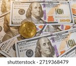 A Bitcoin placed on a stack of hundred dollar bills.