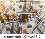 Bitcoin placed on a stack of hundred dollar bills.