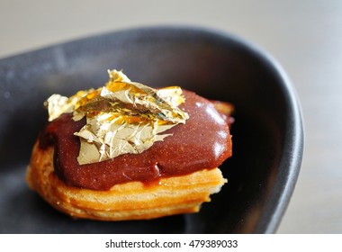 Bite Of A Chocolate Eclair Pastry With An Edible Gold Leaf On Top