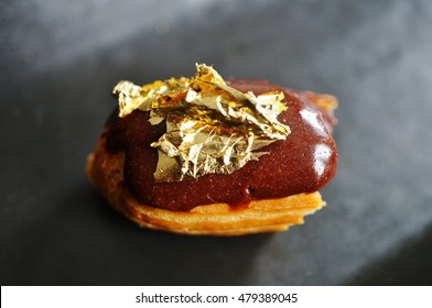 Bite Of A Chocolate Eclair Pastry With An Edible Gold Leaf On Top