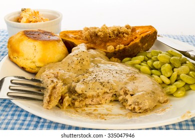 Bite Cut From Country Fried Pork Cube Steak Smothered In Milk Gravy.  Served With Baked Sweet Potato And Lima Beans With Buttered Biscuit And Carrot And Raisin Salad.  Southern Fried Soul Food.