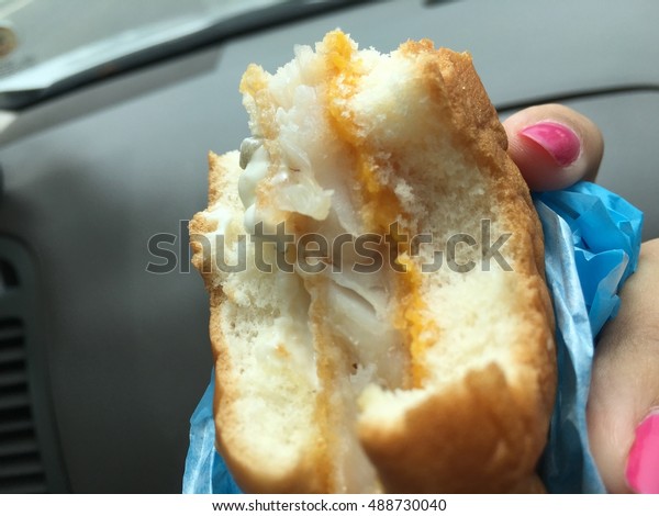 Bite Fried fish burger with a blue wrapped paper in\
lady hand on the way