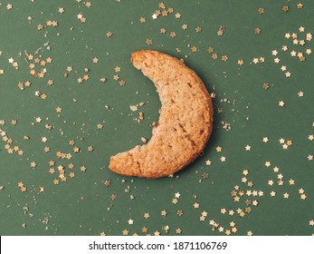 Bite of moon shape cookie biscuit with gold glitter stars on green background. Crescent creative concept. 