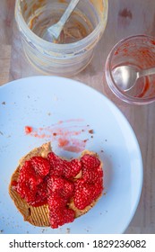 Bite Of Peanut Butter And Raspberry Toast On A White Plate With Empty Peanut Butter And Red Jam Jars.