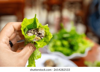 A bite-sized spring roll wrapped in lettuce is held above a table with other greens and dipping sauces in Hanoi on December 29, 2019
