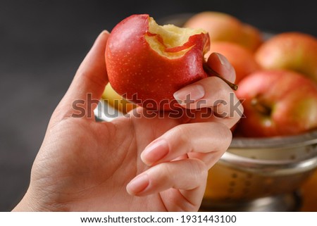 Bitten apple in human hand on metallic bowl full of red ripe apples background. Healthy eating. Apple pie ingridients. Cooking at home