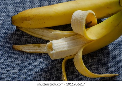Bitten banana next to an unpeeled banana. Partially peeled half eaten ripe yellow banana on white and blue background. Selective focus.