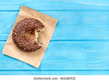 Bitten chocolate donut on paper and a blank wooden background, top view