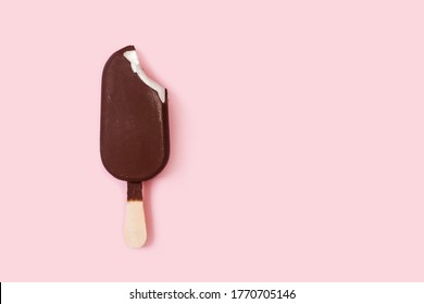 A bitten dark chocolate dipped ice lolly on a pink background