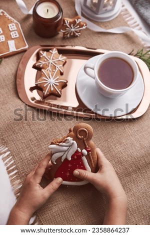 Bitten gingerbread cookie of St Nicholas in child's hands. Atmoshperic seasonal Christmas decorations with cocoa. Traditional holiday in Europe