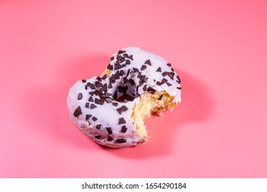 Bitten glazed donut with chocolate chip on top isolated on pink background