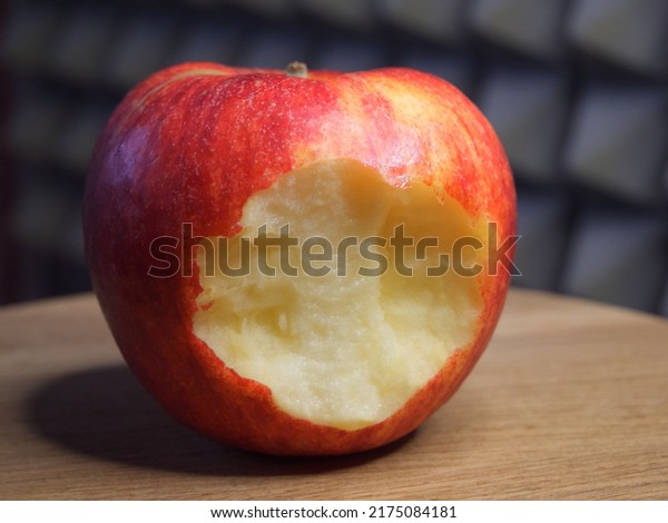 A bitten\
red apple on a wooden surface. Ripe\
apple