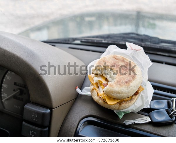 A\
bitten sandwich next to the ignition keys laid on a car dashboard,\
concept of having a coffee break while travel by\
car