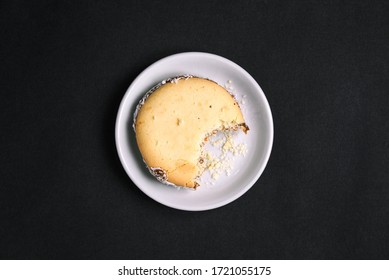 The Bitten-off Cookie Is On A White Plate. Sweet Pastries And Crumbs. Top View On A Black Background. Flat Layout.