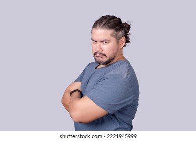 A bitter man in his 30s looking at the camera with a scowling face and arms crossed. Jealousy, displeasure or pettiness. - Shutterstock ID 2221945999