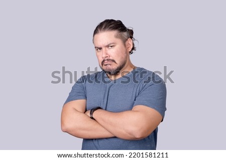 A bitter man in his 30s looks at the camera with a scowling face and arms crossed. Jealousy, displeasure or pettiness.