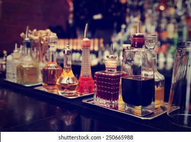 Bitters and infusions on bar counter, bar bottles in blurred background, toned image