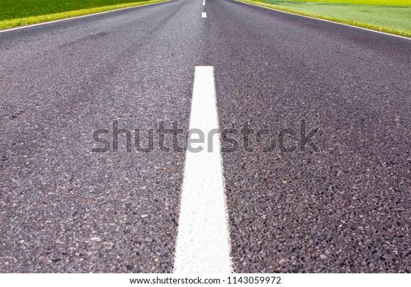 bitumen road markup signs and lines. travelling\
far for long distances hobby concept. car roads in natural\
landscape with green bright fields.\
