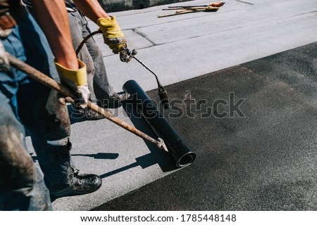 Bituminous membrane waterproofing system details and installation on flat rooftop. Professional construction worker  installing and waterproofing flat roof at house construction site. 