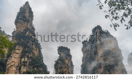 Bizarre cliffs against a cloudy sky. Green vegetation on steep rocky slopes. Sharp peaks. China. Zhangjiajie 