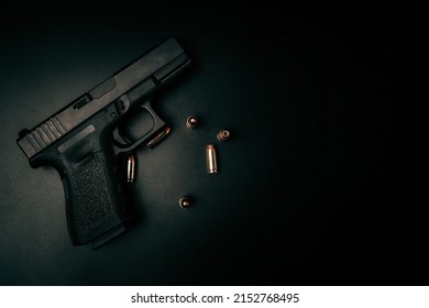 A black 9mm pistol on a black background with 9mm ammunition next to it. top view