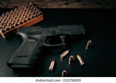 A black 9mm pistol on a black background with a box of 9mm ammunition next to it. top view