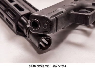 A black 9mm pistol on top of a black AR 15 .223 caliber rifle with a white background