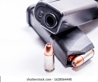 A black 9mm semi automatic pistol with a loaded pistol magazine with a single 9mm hollow point bullet on a white background