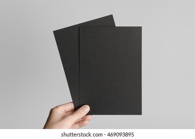 Black A5 Flyer / Invitation Mock-Up - Male hands holding black flyers on a gray background.