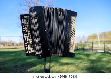 A black accordion is sitting on a grassy field. The accordion is open and has a white and black design. The scene is peaceful and serene, with the accordion standing out against the green grass - Powered by Shutterstock