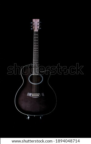 black acoustic guitar with a white profile around it on a black background, placed on a stand in a vertical position, copy space low key