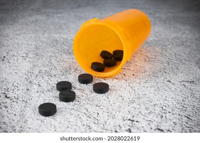 Black Activated Charcoal Pills Scattered From Orange Prescription Bottle On Gray Surface