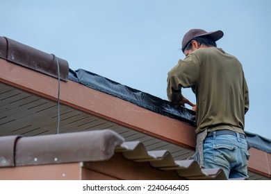 Black adhesive tape for hermetic joints of roofing materials, when mounting the roof, Tool for waterproofing on a background of roof.Asian worker installing bitumen foil on the roof.