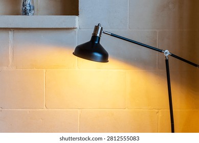 Black Adjustable Desk Lamp Casting Warm Light on Textured Stone Wall in Cozy Interior