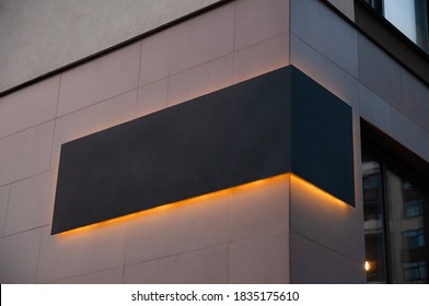 black advertising board with yellow led glow  on the corver of building, company sign on wall. Place for text